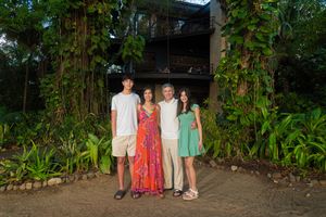 Family of four posing together outside a lush tropical resort surrounded by greenery.