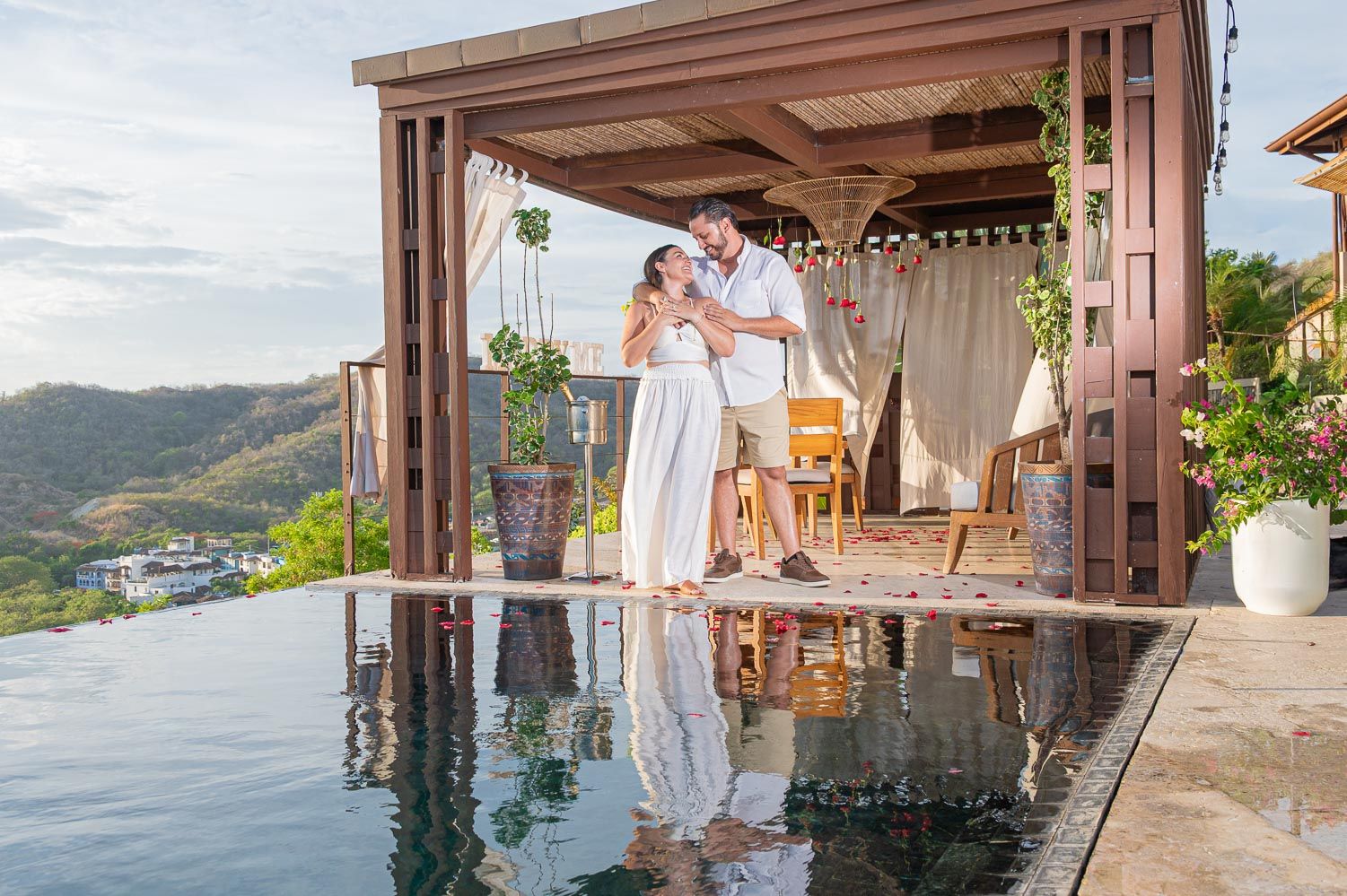 Couple embracing on a luxury infinity pool terrace with stunning tropical hillside views at a romantic resort.