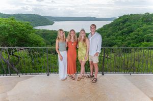 Four people posing on a scenic overlook with lush green jungle and a tranquil lake in the background.