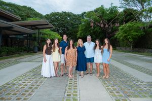 A happy family of eight poses together on a stone pathway surrounded by lush tropical greenery.