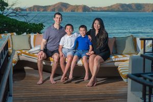 Family of four sitting together on an outdoor deck with a scenic ocean and mountain view at sunset.