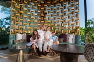 Family of four smiling together on a luxury resort sofa with ornate golden wall decor in a tropical setting.