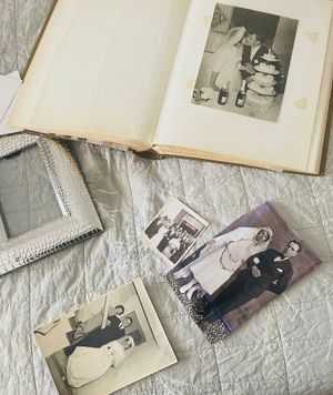 Vintage black and white photographs and an old photo album lay scattered on a textured gray surface.