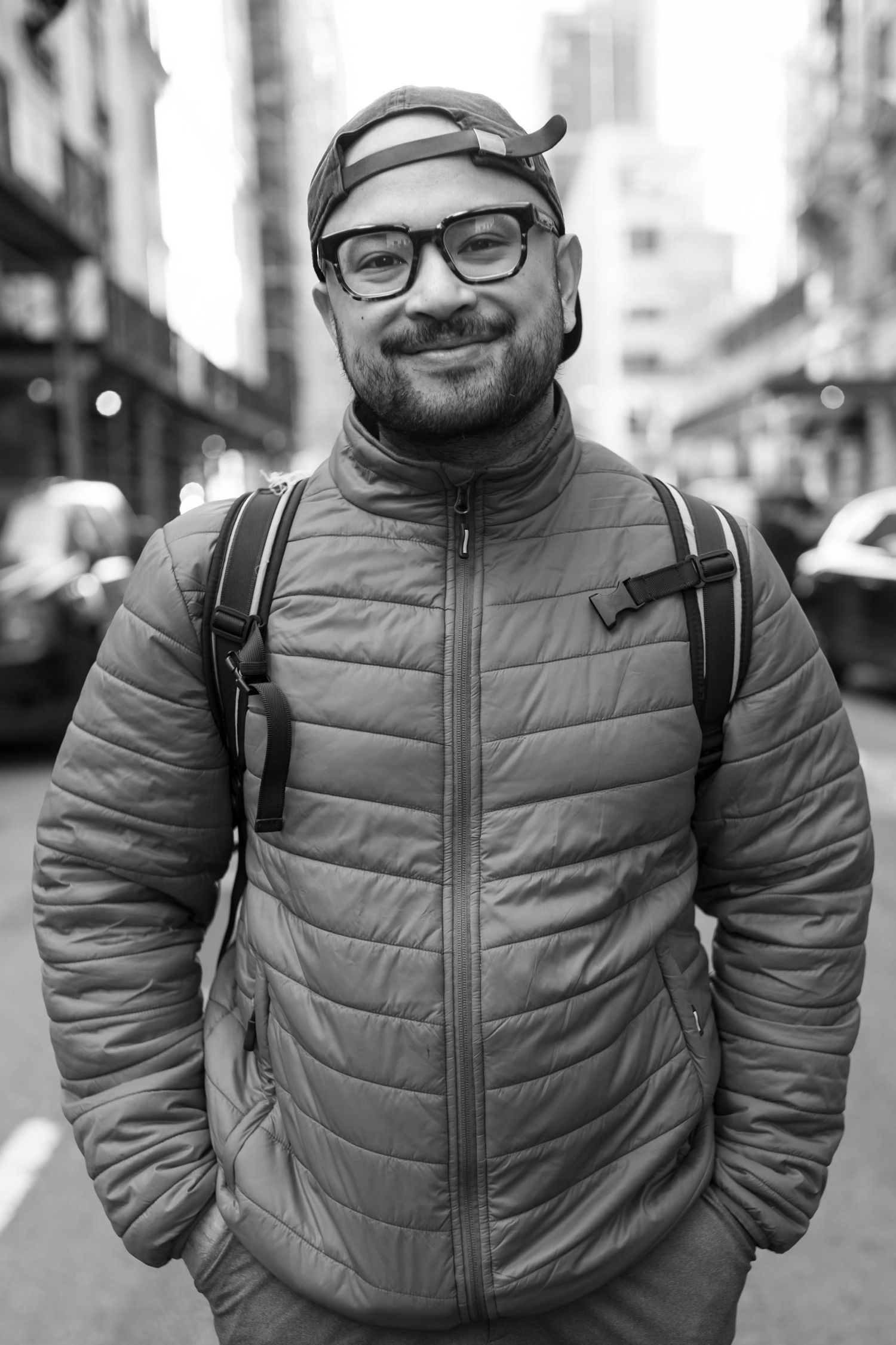 A person in a bright red puffy jacket and glasses poses on an urban street.