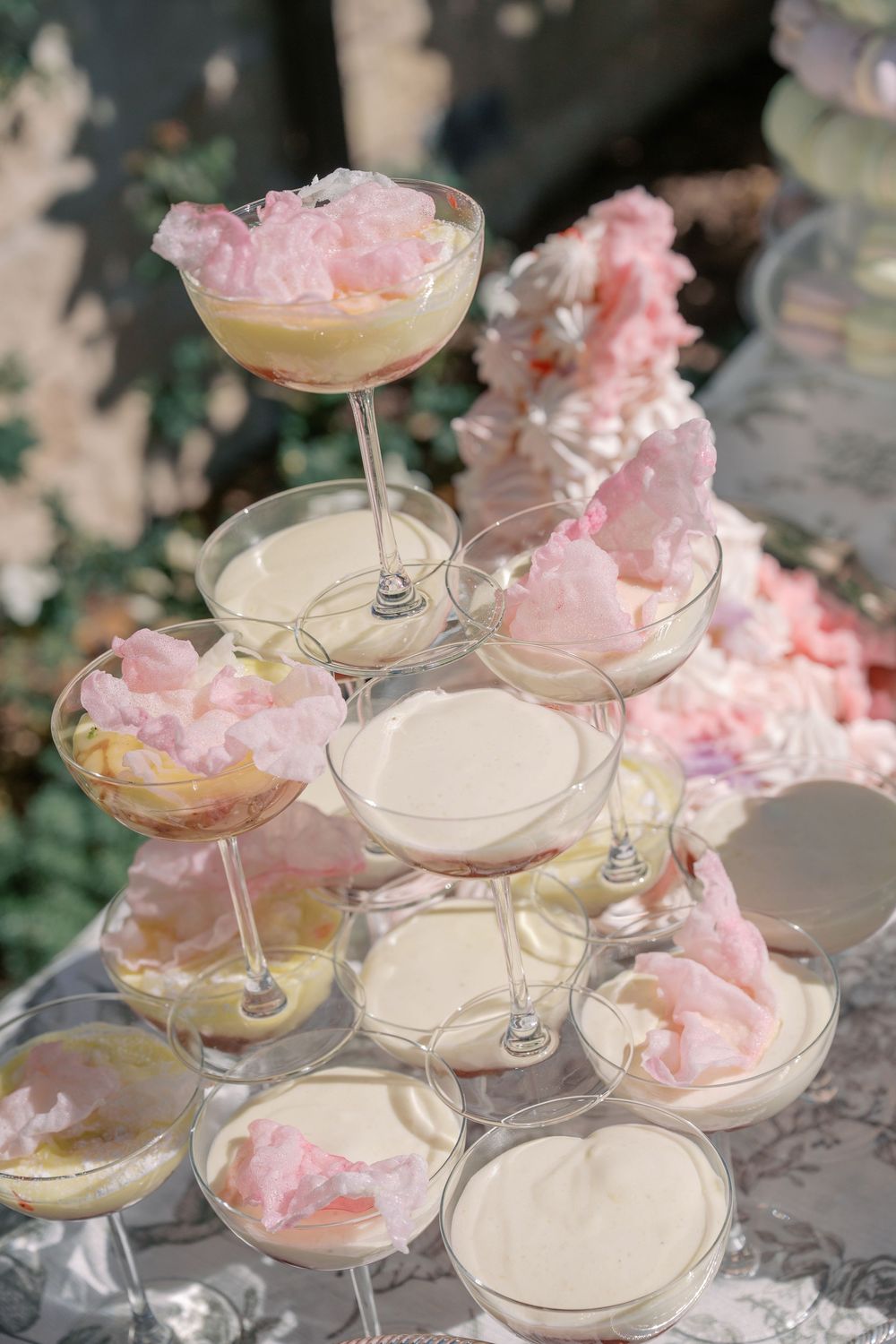 Tiered display of pink cotton candy garnished cocktails in coupe glasses arranged on a mirrored surface.