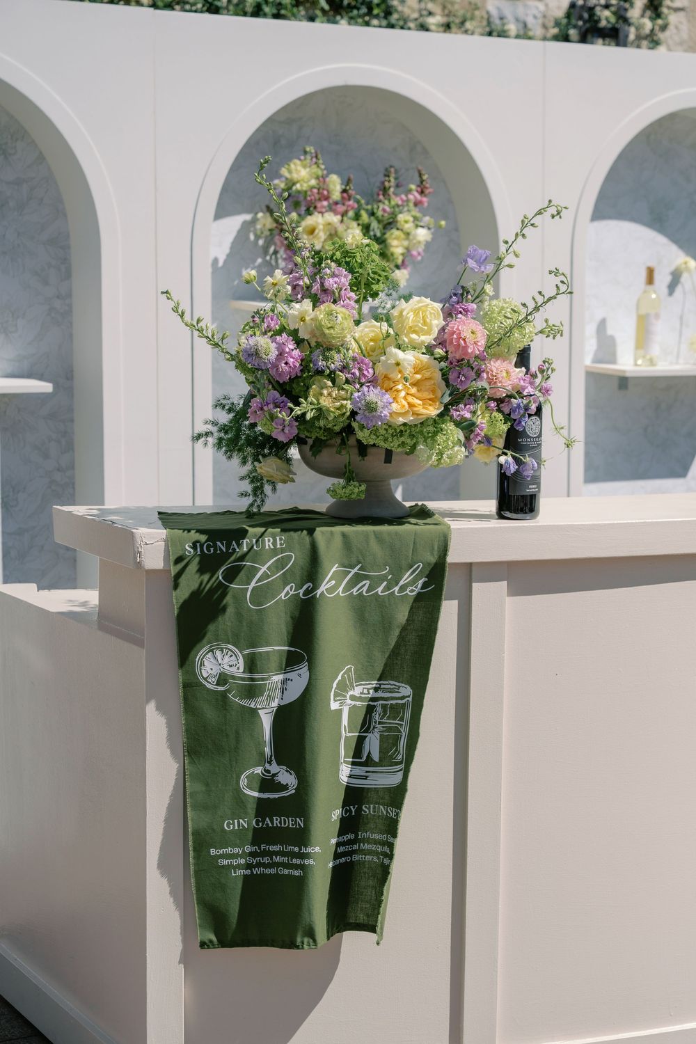 A series of elegant floral arrangements in green vases displayed against white arched alcoves with natural lighting.
