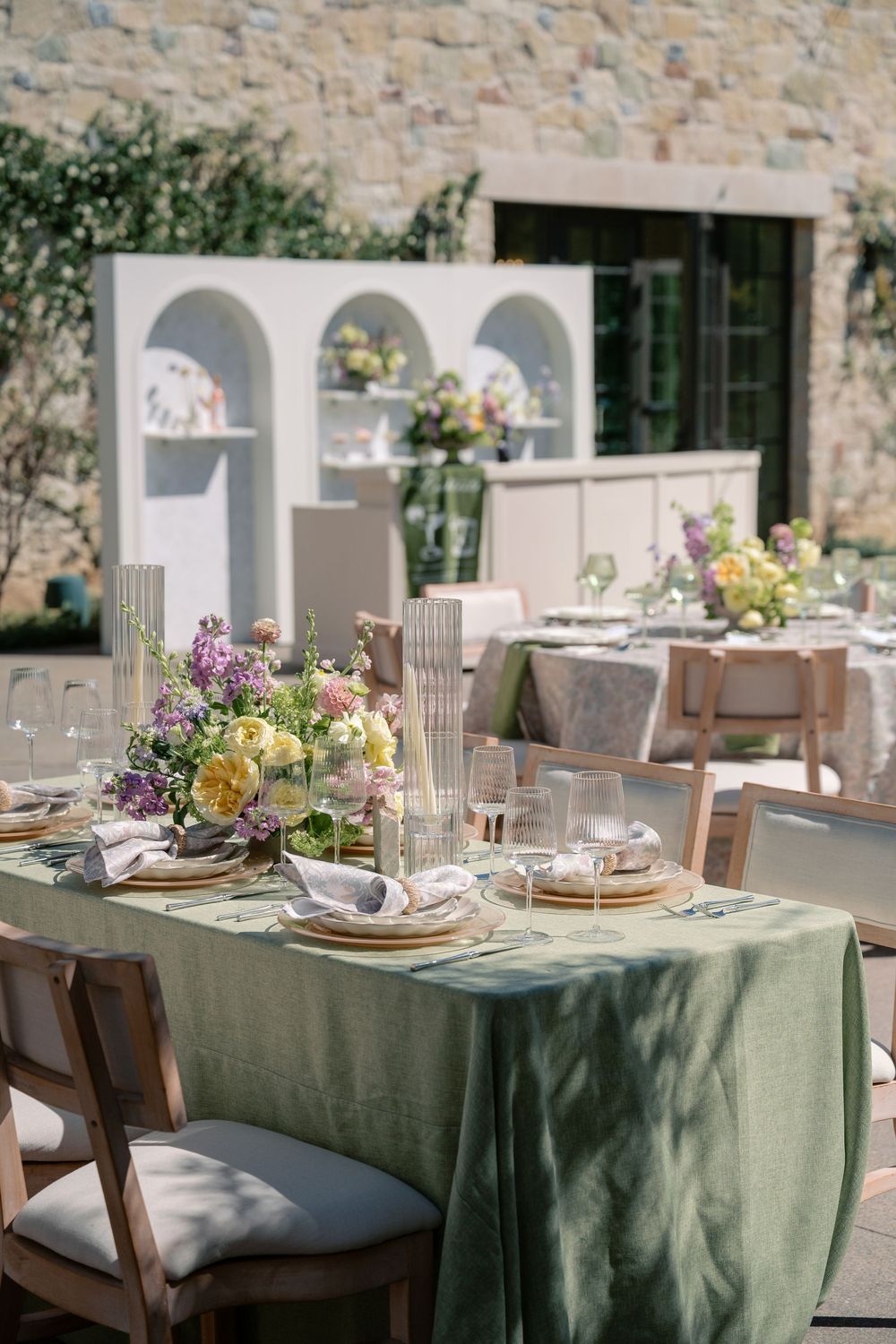 Elegant dining tables set with sage green tablecloths, floral centerpieces, and place settings in a stone-walled venue.