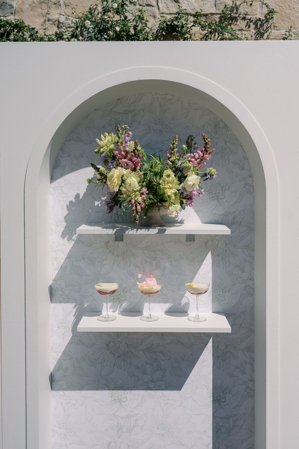 White arched wall niches decorated with floating shelves displaying floral arrangements and glassware.