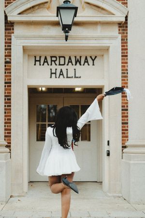 Three white dresses flutter in motion against a brick building entrance marked Hardaway Hall.
