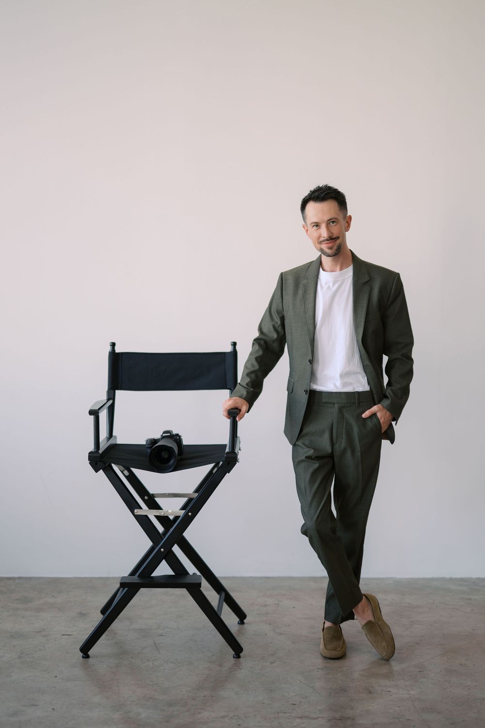 A series of five images showing someone in a suit standing next to a black director's chair in various positions.