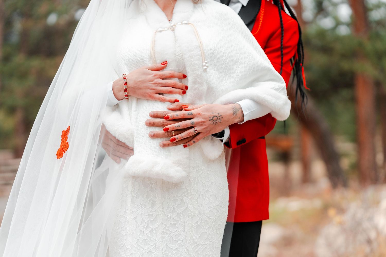 Bride and groom embracing outdoors, bride in white lace gown with veil and fur wrap.