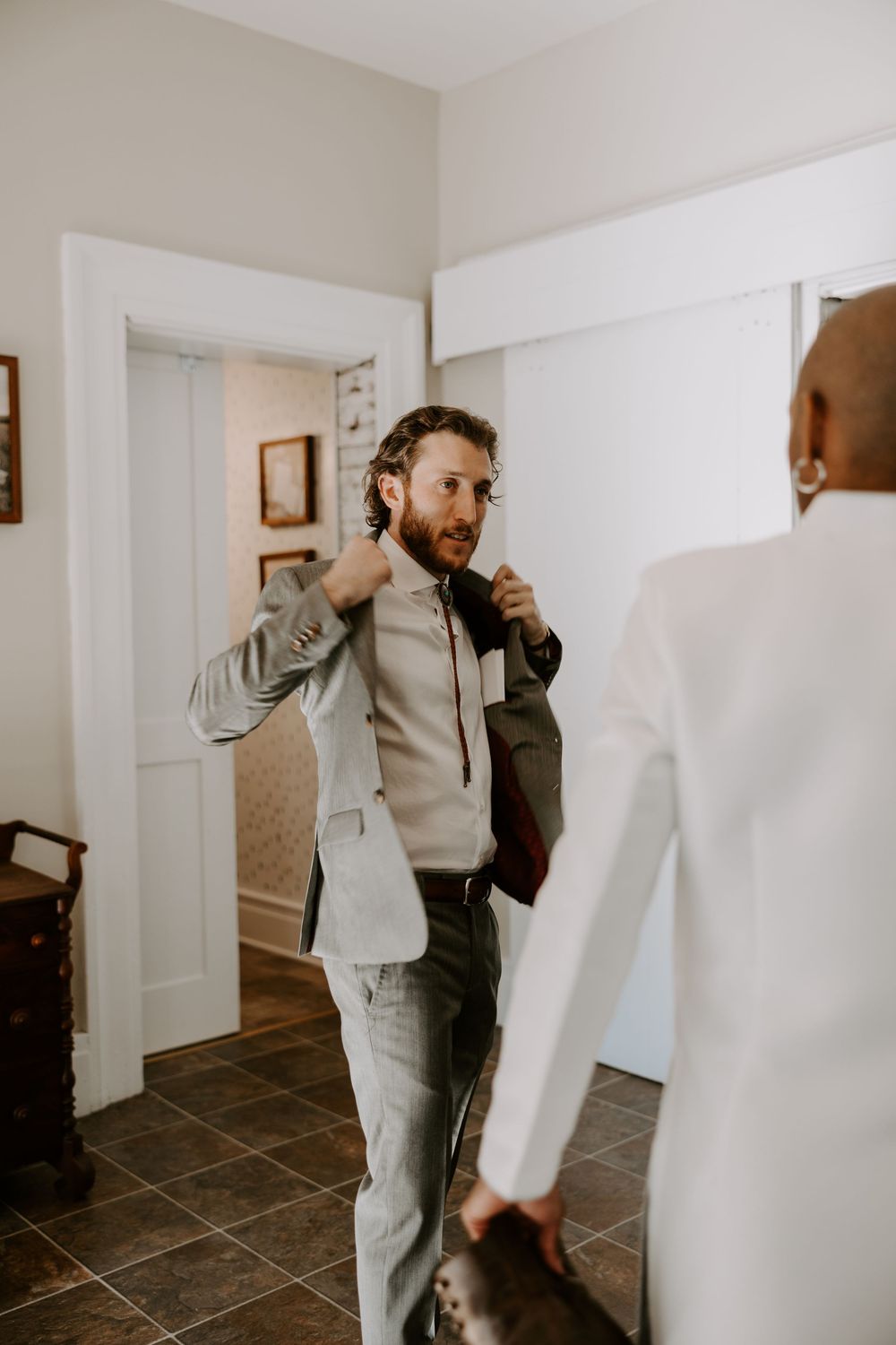 Groom in light gray suit adjusting jacket while getting ready with wedding party before the ceremony.