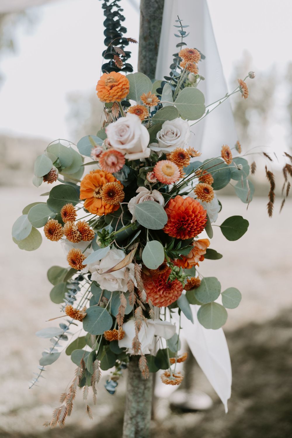 Stunning wedding arch floral arrangement featuring orange zinnias, blush roses, and eucalyptus greenery.