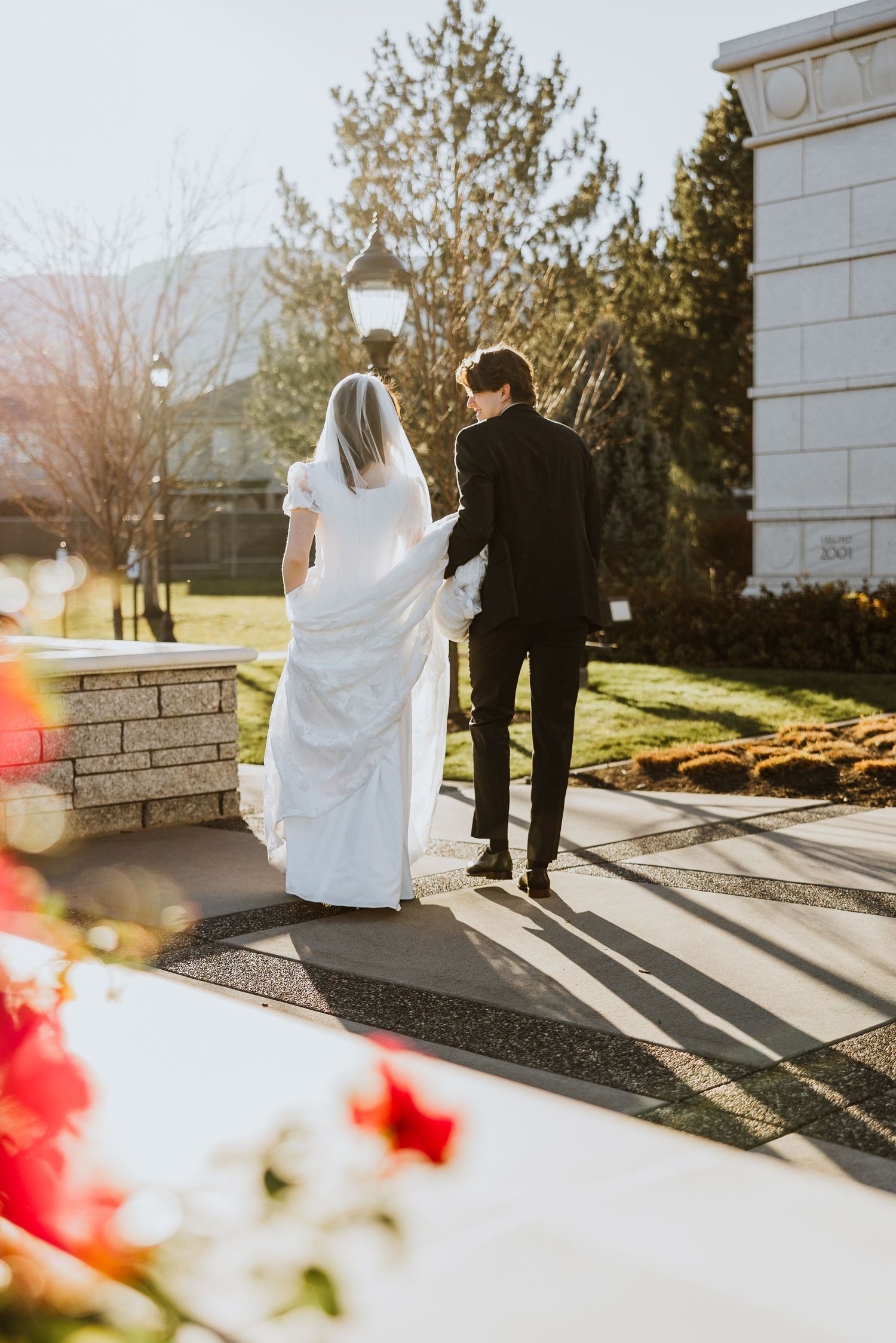 A bride and groom walk away towards the sunshine with pink flowers in the foreground