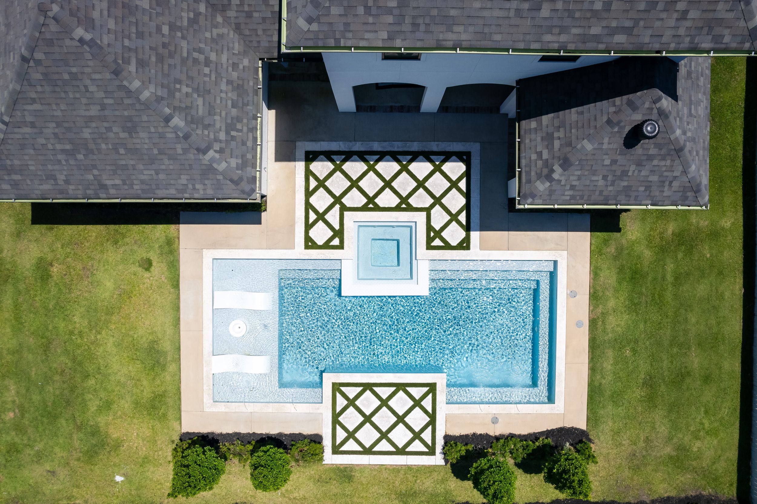 Aerial view of a residential neighborhood showing rooftops, swimming pools, and green lawns from above.