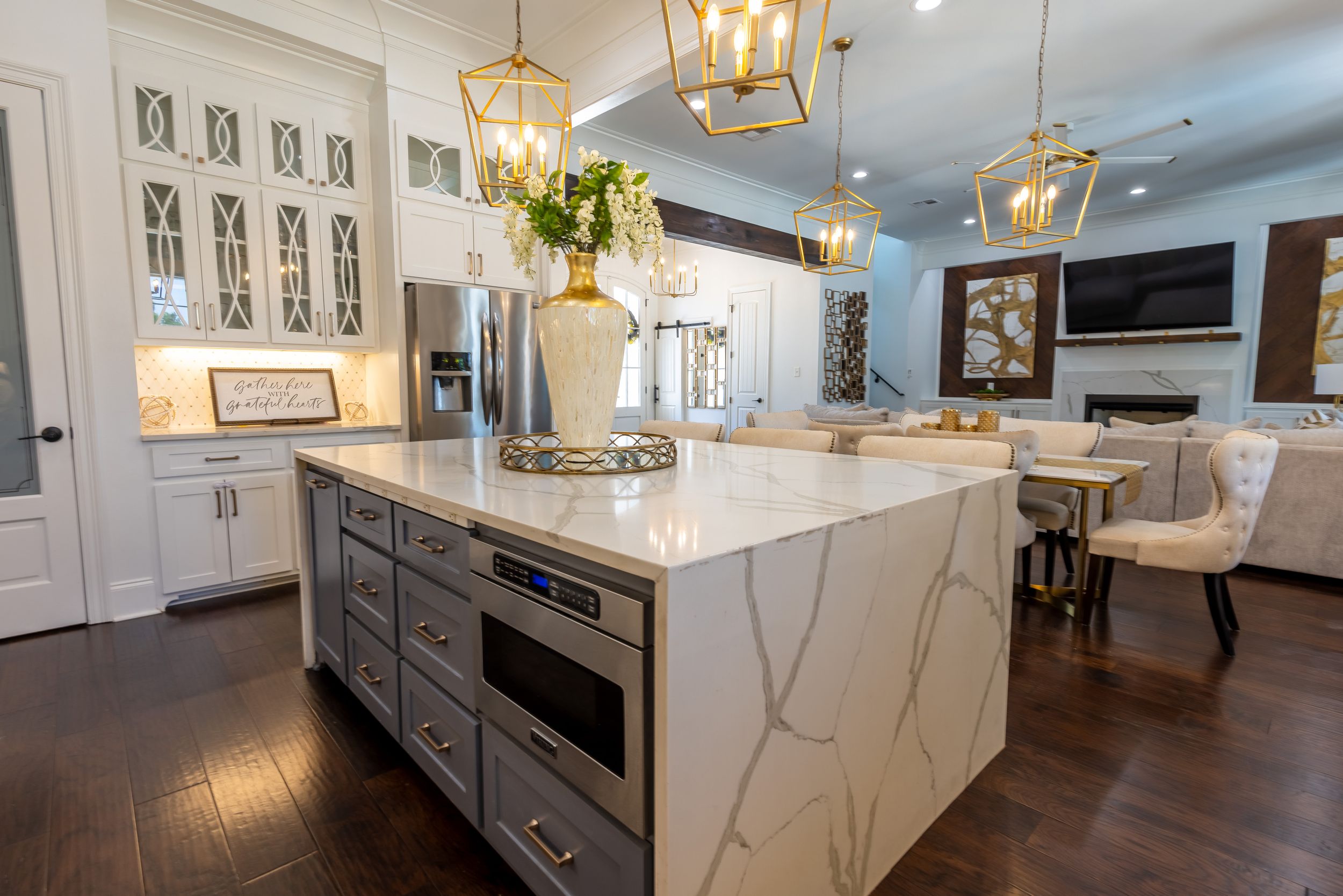Modern white kitchen with gold pendant lights features marble countertops and dark wood floors in an open concept layout.