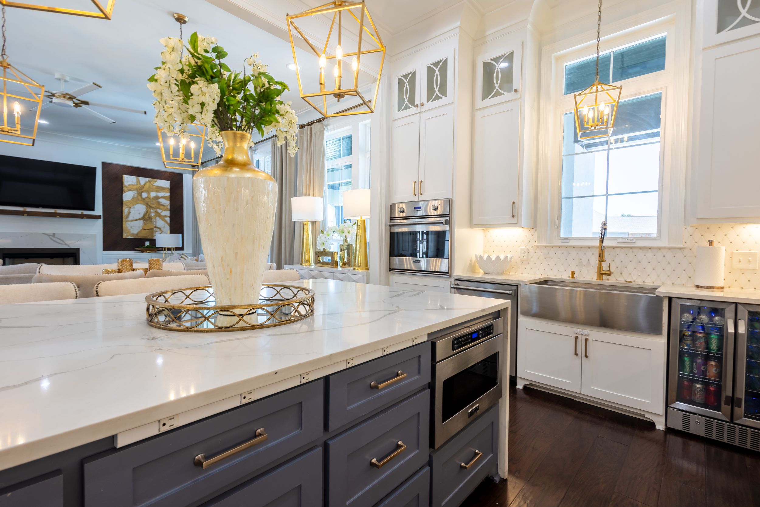Modern white kitchen with dark base cabinets, gold hardware, marble countertops, and pendant lighting creates luxurious appeal.