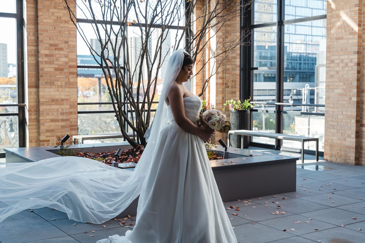 A bride in a flowing white gown poses in an elegant indoor venue with brick walls and large windows.