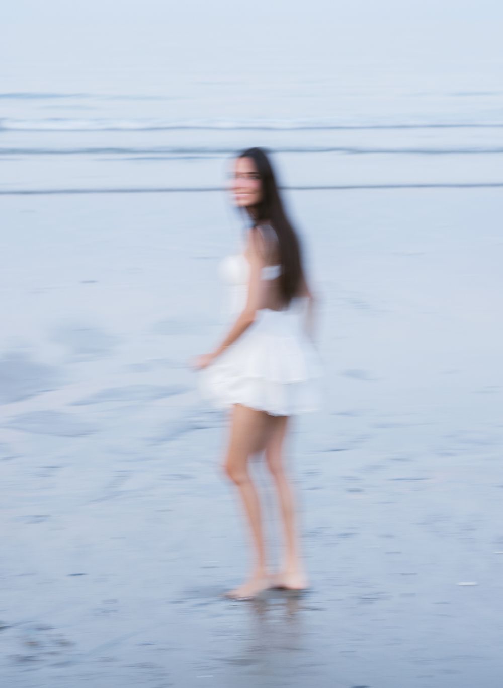 Slow shutter, blurry photos during senior portrait photos of senior girl in white dress swaying in ocean. Hampton senior photographer.