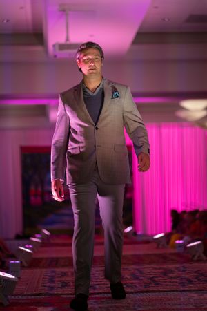 Gentlemen’s Corner model walks down the pink-lit runway wearing a gray suit during the Azalea spring fashion show 2026