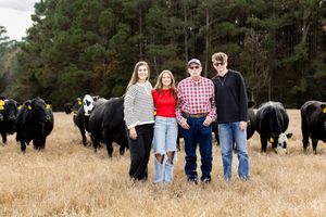 Group photo of people arranged in a line with pine trees and grazing buffalo in the background.