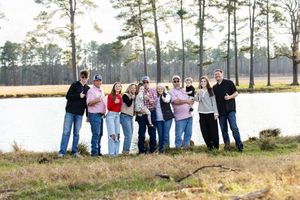 Family members lined up casually along a scenic lakeside with pine trees.