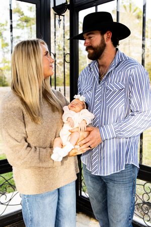 Family portraits in a sunroom showing tender moments with their newborn baby.