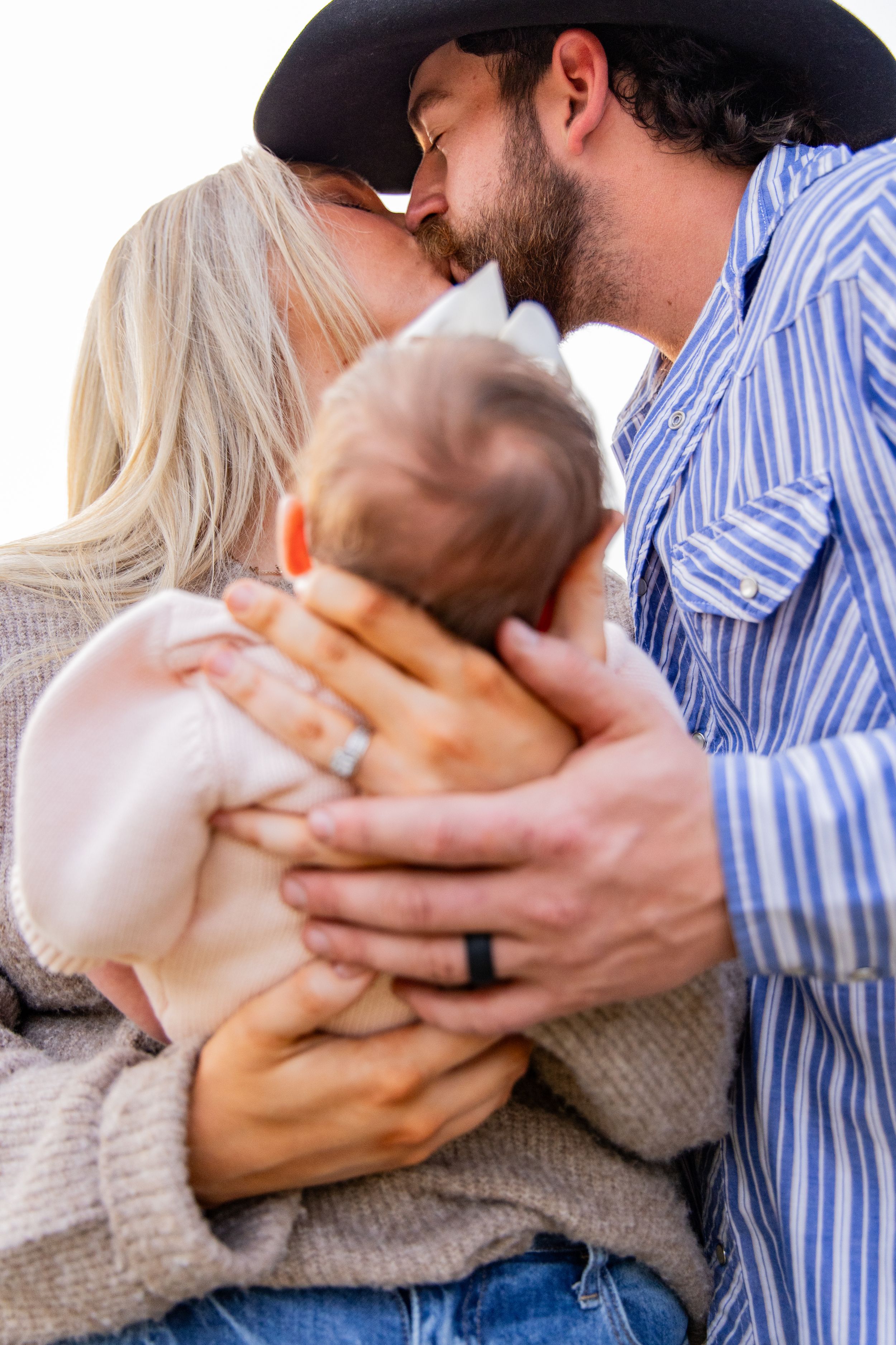 Parents sharing intimate moments with their newborn baby against a natural outdoor backdrop.