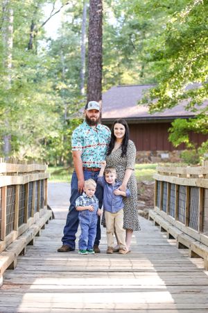 Candid family moments captured on a wooden bridge walkway in a wooded park setting.