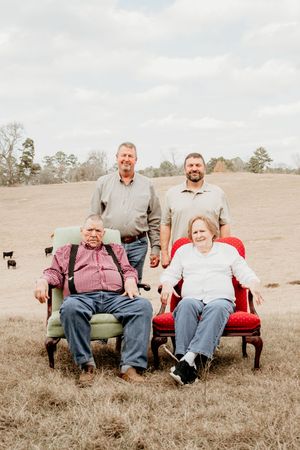 People seated on a red vintage couch placed in an open field landscape.