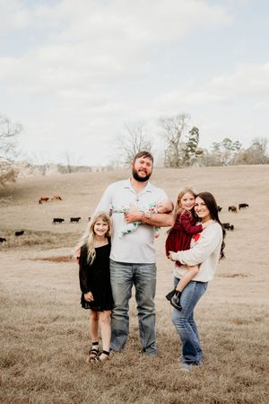 A playful family photo session in a rustic field with cattle grazing in the background.