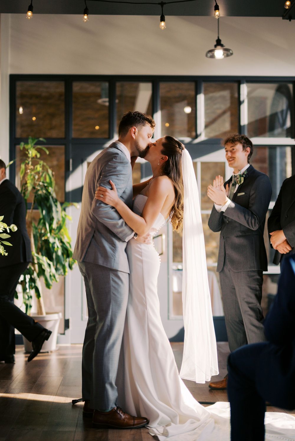 Wedding party members share intimate moments in an elegant indoor venue with pendant lighting.