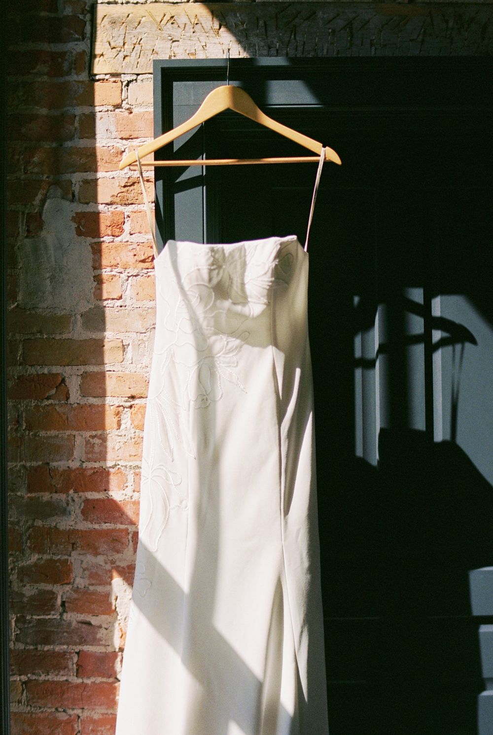 White wedding dress hangs elegantly against exposed brick wall in dramatic lighting.