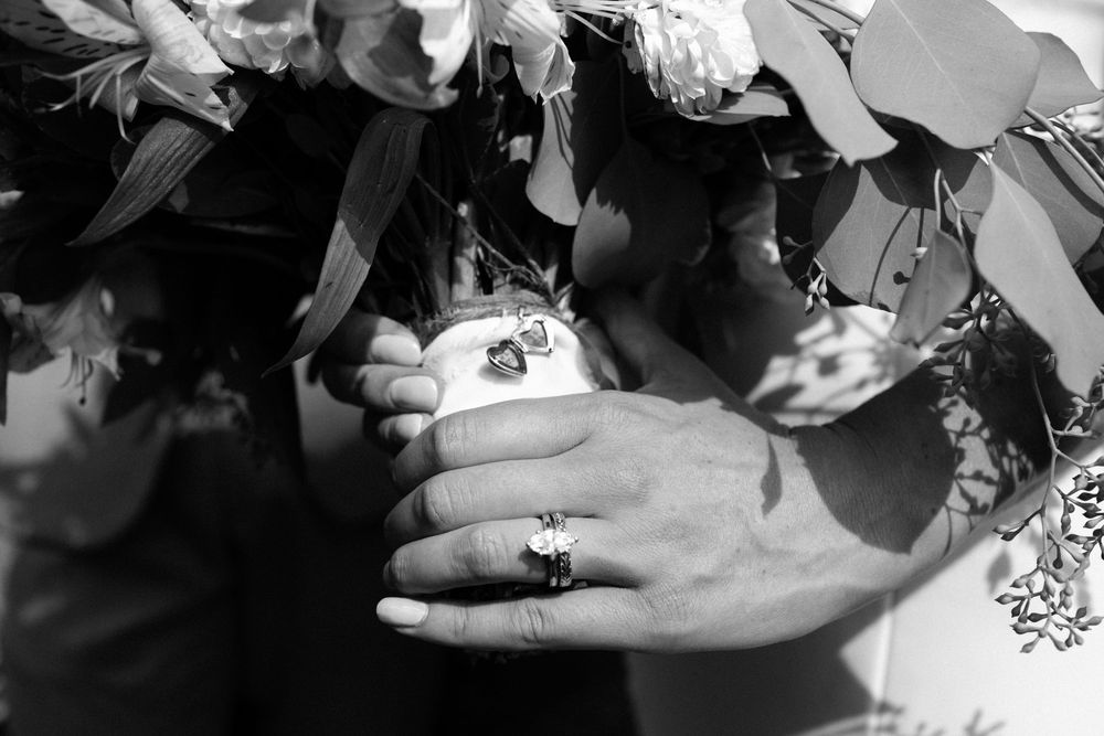 Black and white image of hands holding a delicate butterfly while sunlight filters through leaves in the background.