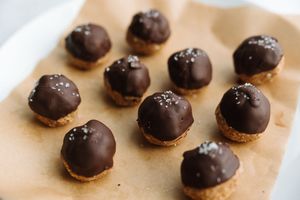 Chocolate-dipped energy balls with sea salt on parchment paper baking sheet.