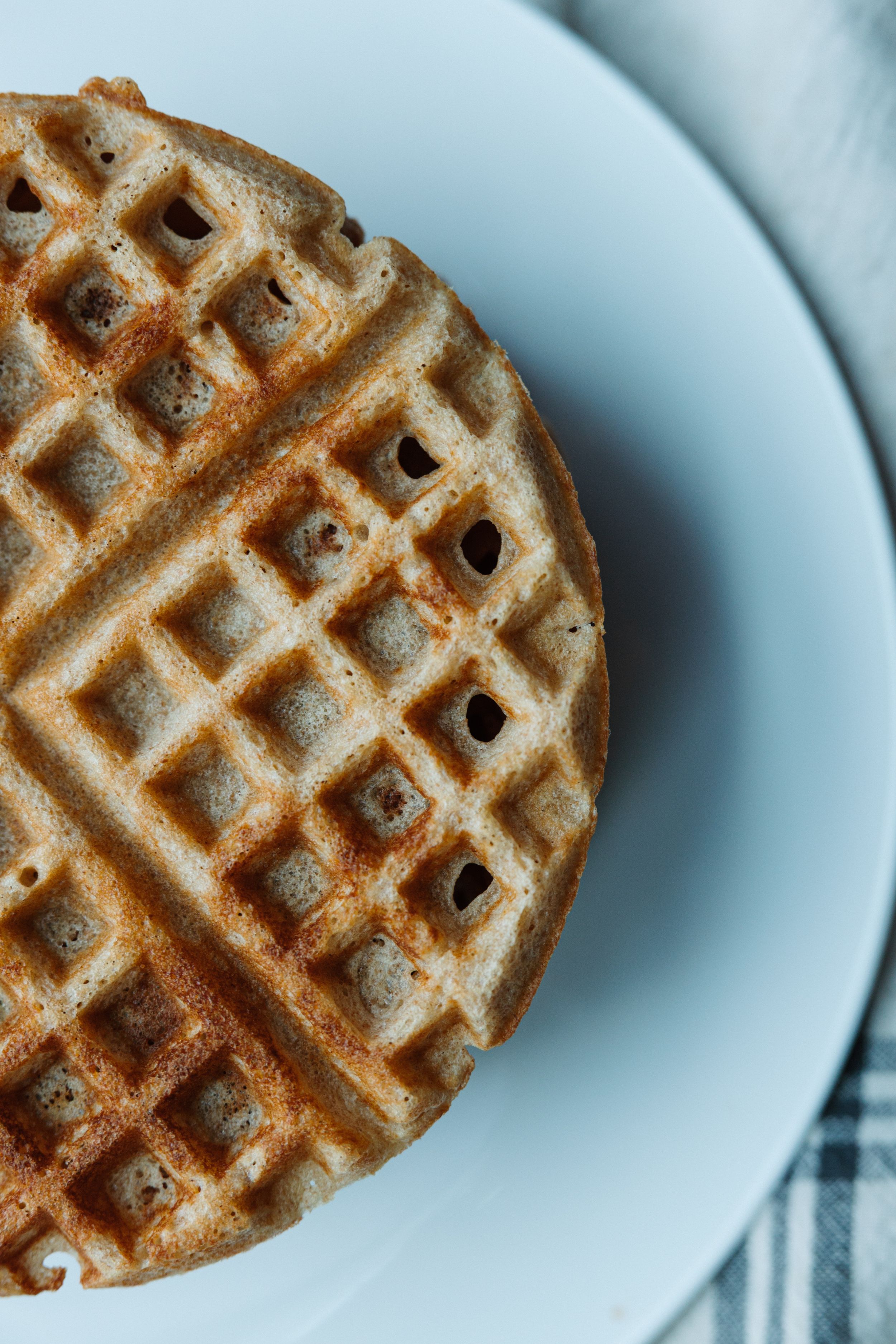 Close-up of golden round waffle on white plate with checkered cloth.