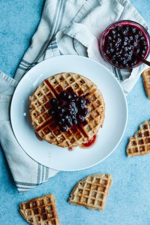 Overhead view of a single waffle topped with blueberry jam on white plate with linen napkin.