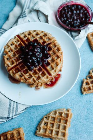 Homemade waffle topped with blueberry jam on white plate with blue background.