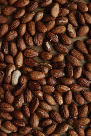 Top-down view of a large pile of roasted almonds spread across a wooden surface.