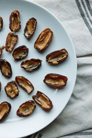 Overhead view of peanut butter-filled dates arranged on a white plate with striped linen.