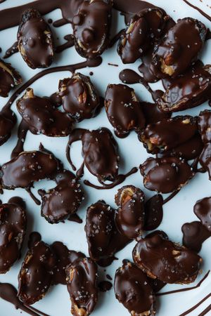 Overhead view of chocolate-dipped date and nut clusters with sea salt on a light plate.