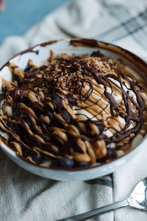 Bowl of yogurt topped with granola, peanut butter, and chocolate drizzle on a linen cloth.