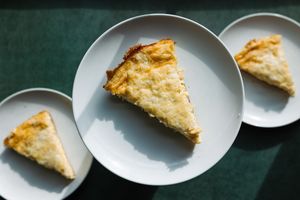 Three triangular slices of golden pastry or pie served on separate white plates on green surface.