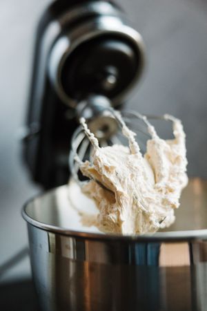 Stand mixer whipping creamy white dough or batter in a stainless steel bowl.