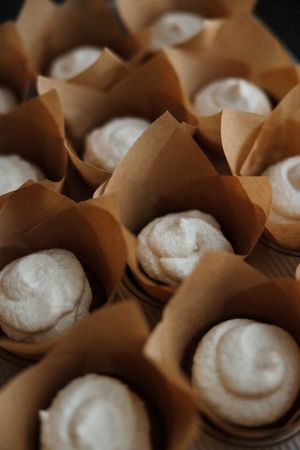 Rows of white meringue cookies in brown parchment paper liners on a tray.