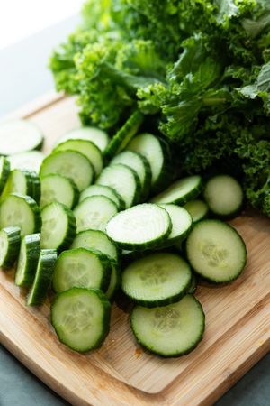Sliced cucumbers and fresh kale on a wooden cutting board for green juice.