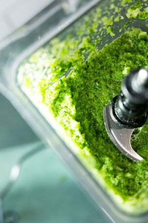 Blended green vegetables in a blender showing vibrant kale smoothie mixture.