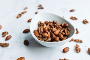 Mixed roasted almonds and walnuts in a white bowl on a marble surface.
