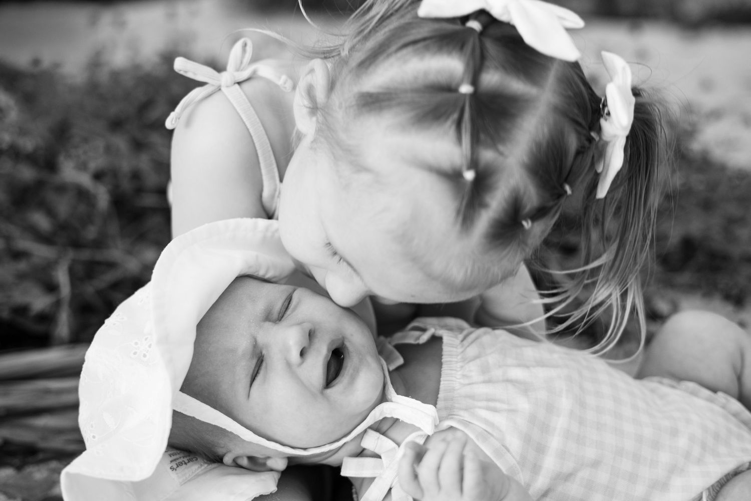 Black and white photo of a young girl kissing a newborn baby sibling on the forehead at Coquina Beach Florida
