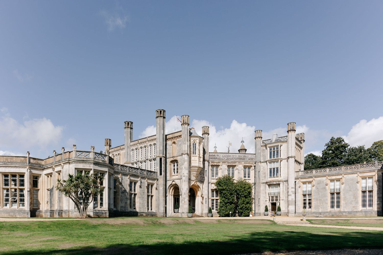 Gothic stone castle with ornate architectural details and towers stands majestically against a blue summer sky. Highcliffe Castle Dorset
